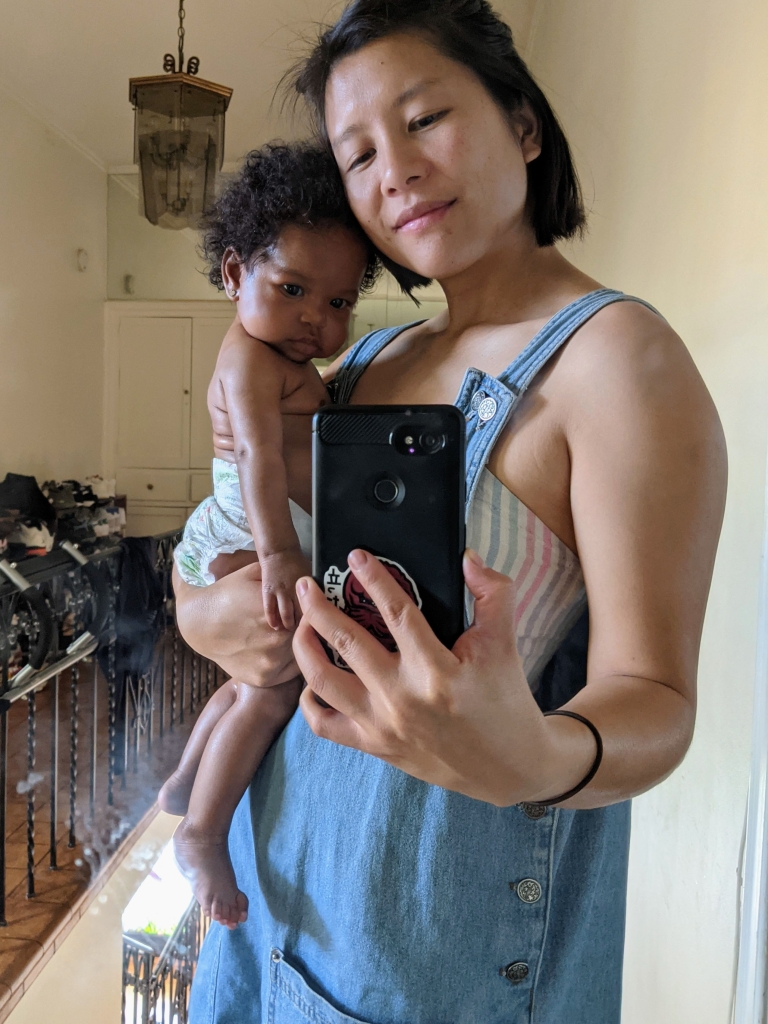 LA doula Priscilla Hsu, an olive skin tone Taiwanese femme with really dope demi-lids and small dimples by the corners of her mouth, carries a baby of Black excellence and model caliber in their right arm. The baby is wearing a diaper and the comfort of its own skin.
